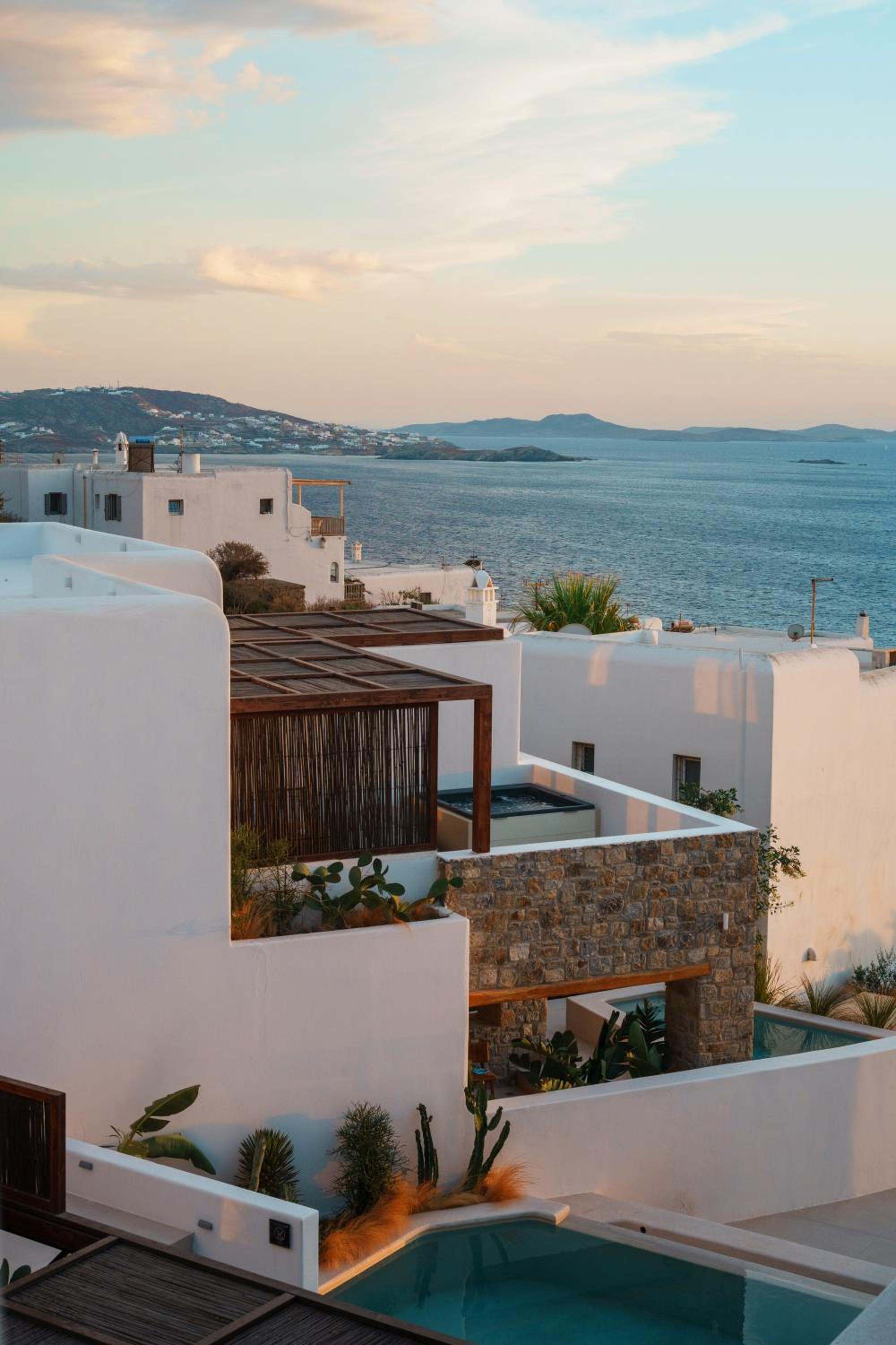 Whitewashed volumes, stone walls and a timber pergola above the bay at dusk