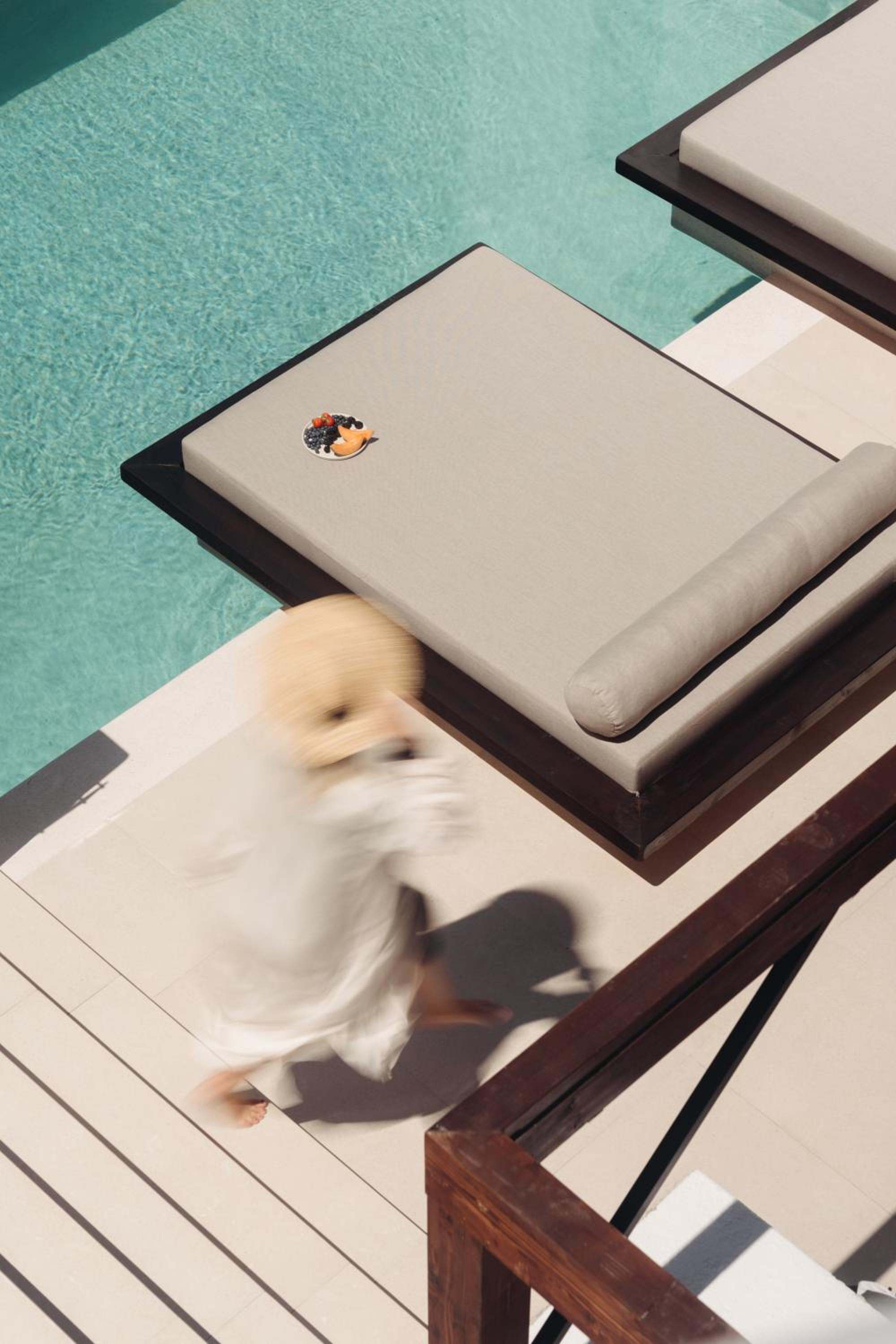 Seen from above, a guest in white walks past a poolside daybed