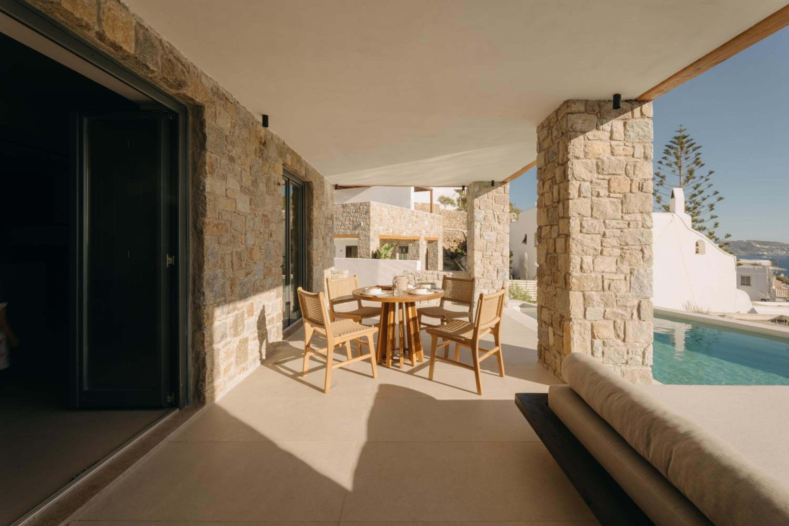 A covered stone terrace with a dining table, next to a pool