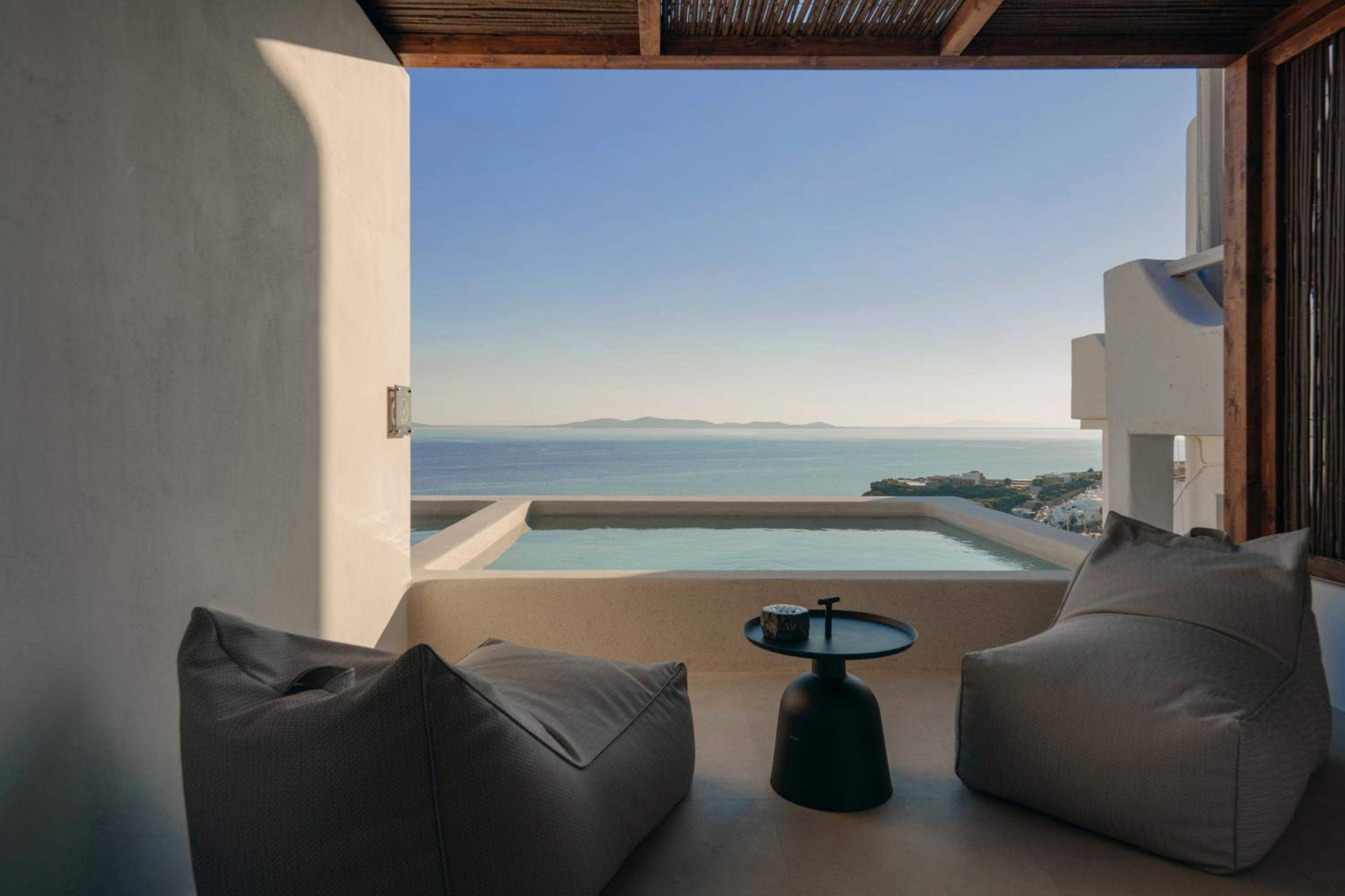 Low cushions and a side table on a covered terrace looking over a plunge pool to the sea