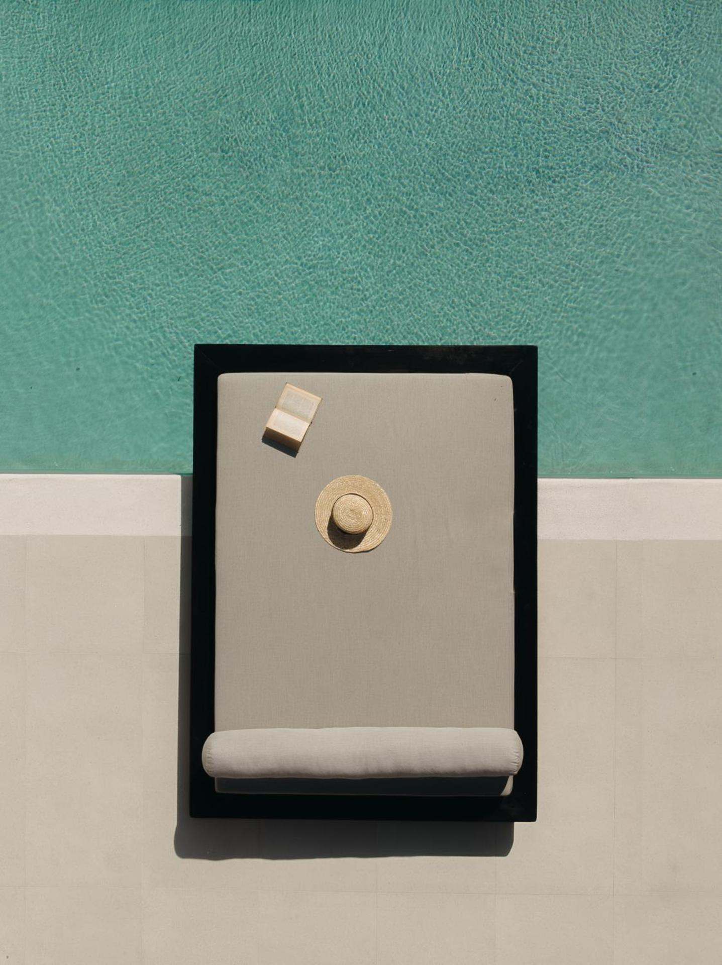 Seen from above, a daybed with a straw hat beside a turquoise pool