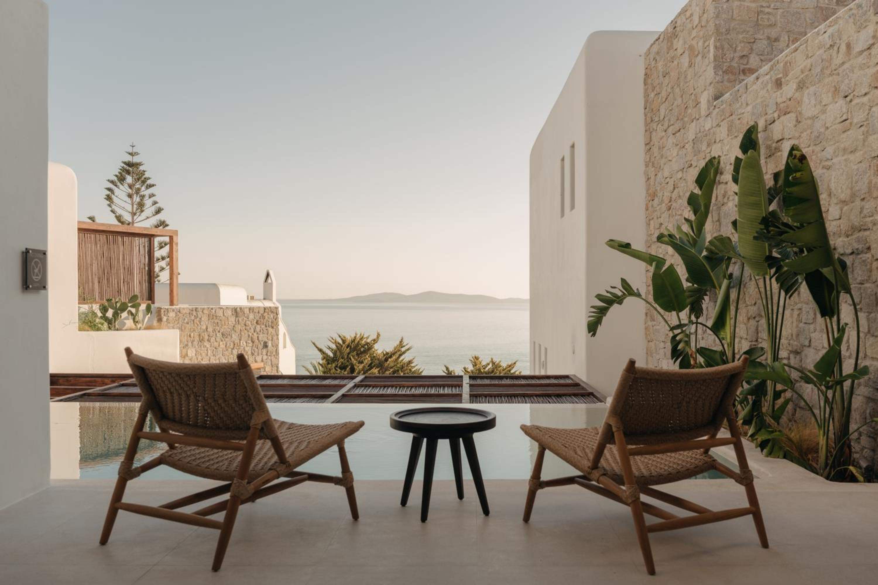 Two woven lounge chairs on a terrace, a plunge pool and the sea framed between whitewashed and stone walls