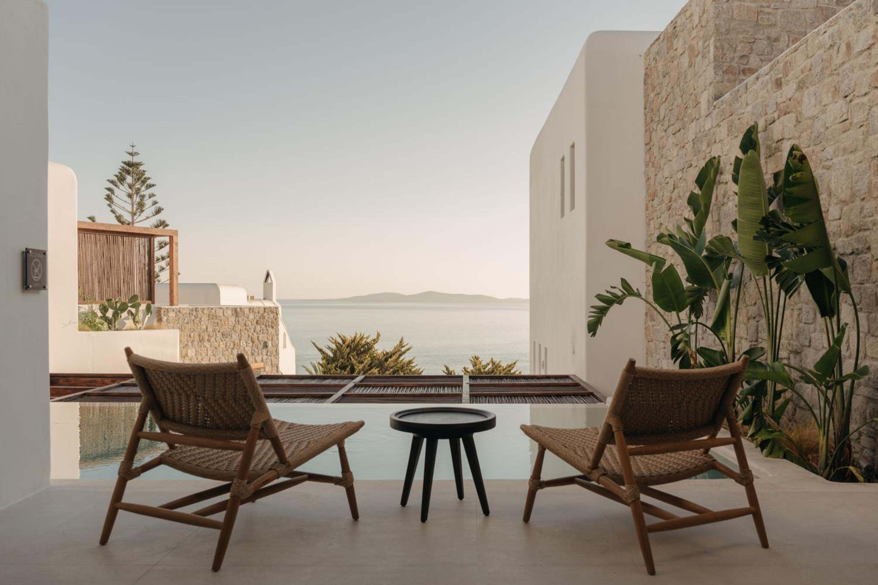 Two woven lounge chairs on a terrace, a plunge pool and the sea framed between whitewashed and stone walls