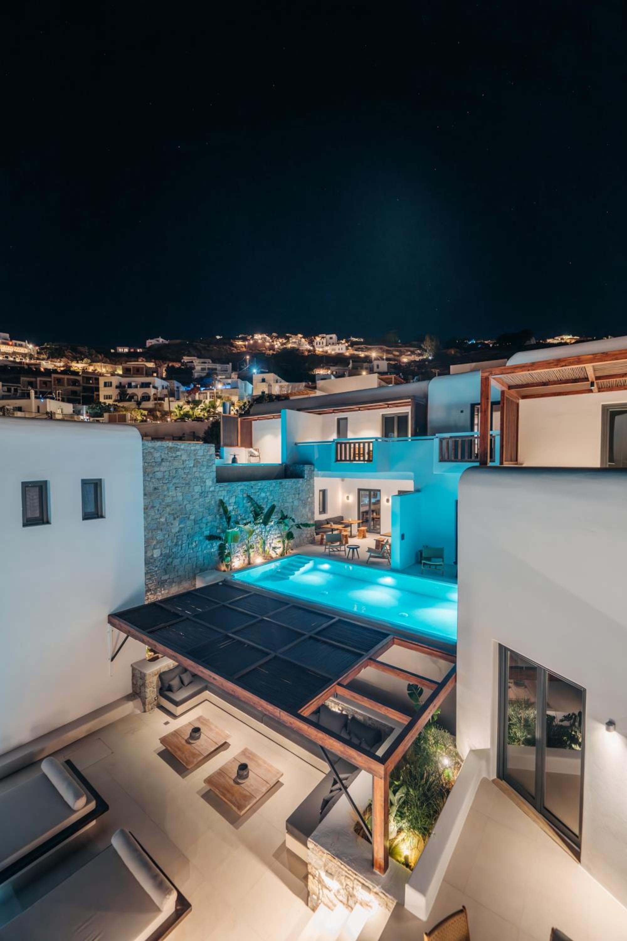 The lit pool and pergola from above at night, with the hillside lights beyond