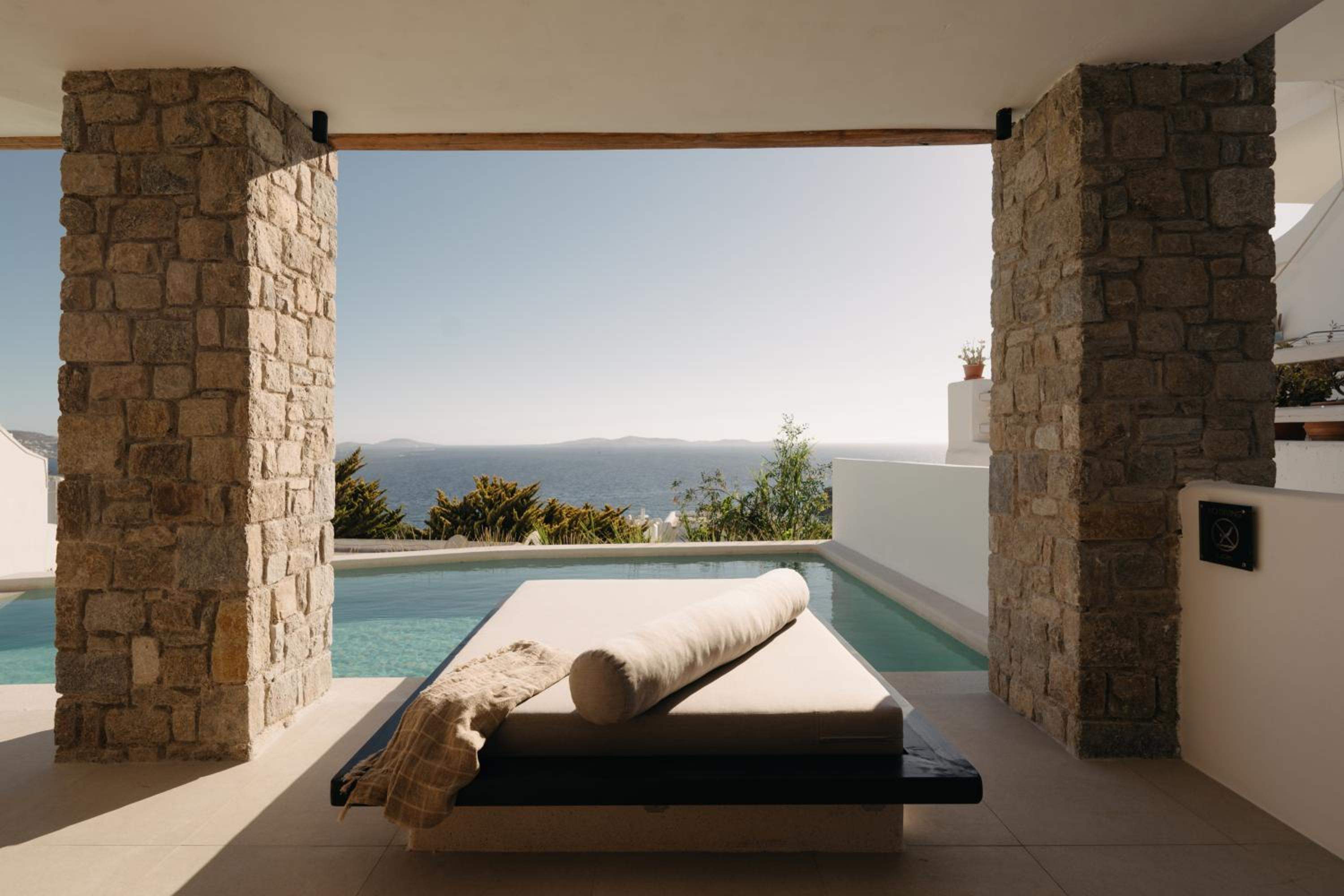 Premier Suite: a daybed beside the private pool, framed by stone columns, with the sea beyond