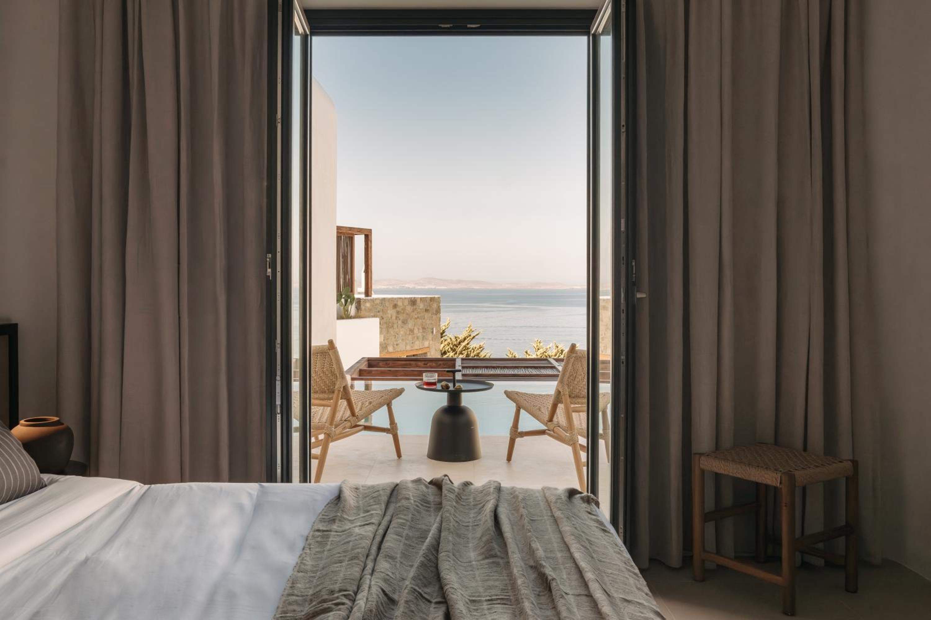 Deluxe Room: the bed, with doors open to a terrace, the pool and the sea